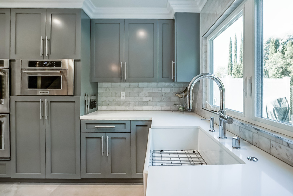 Design ideas for a large transitional l-shaped open plan kitchen in Los Angeles with a farmhouse sink, shaker cabinets, grey cabinets, quartz benchtops, grey splashback, marble splashback, stainless steel appliances, porcelain floors, with island and white floor.