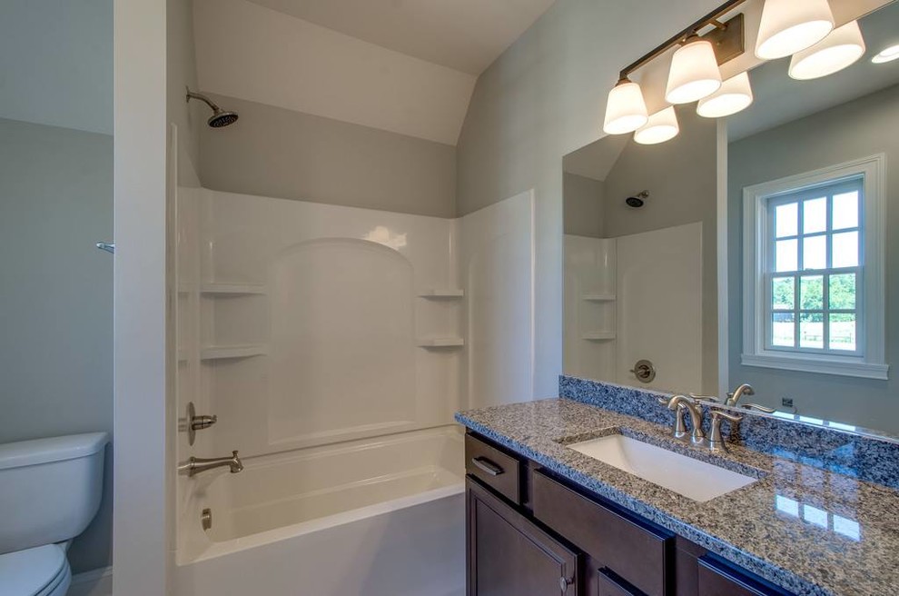 Mid-sized transitional 3/4 gray tile and porcelain tile porcelain tile and gray floor corner shower photo with recessed-panel cabinets, black cabinets, beige walls, an undermount sink, granite countertops and a hinged shower door
