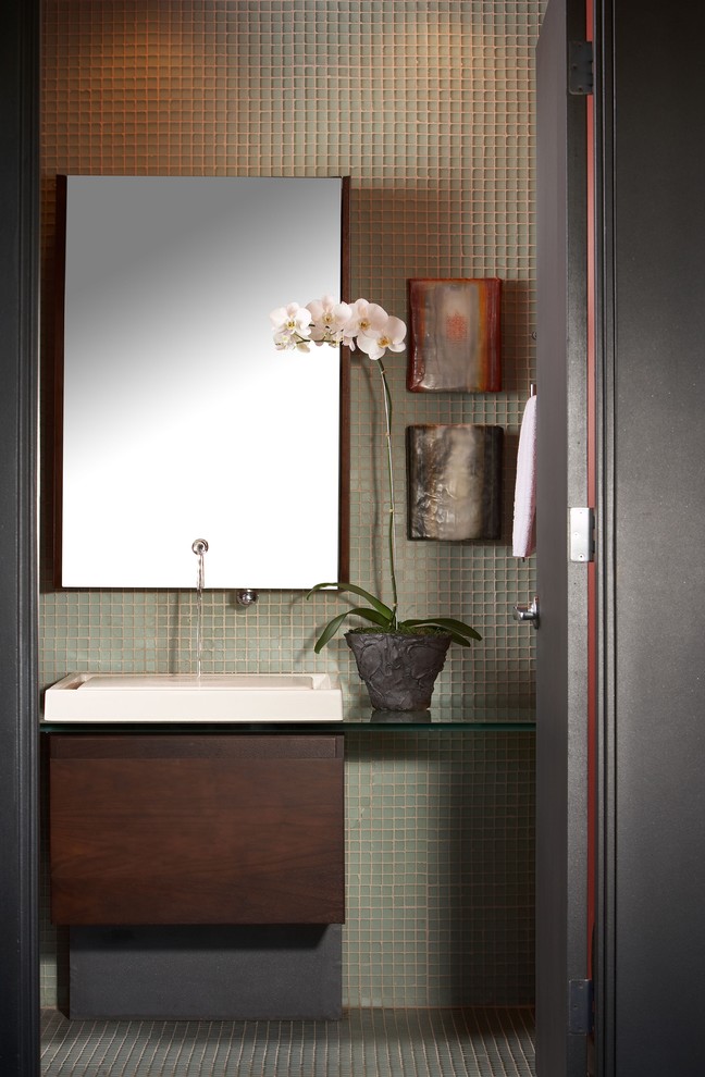 Photo of a mid-sized contemporary powder room in Phoenix with a vessel sink, flat-panel cabinets, dark wood cabinets, glass benchtops, a two-piece toilet, green tile and grey walls.
