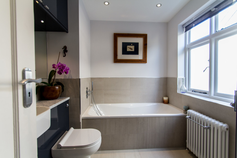 Photo of a mid-sized contemporary bathroom in London with a drop-in sink, flat-panel cabinets, grey cabinets, granite benchtops, a drop-in tub, an open shower, a one-piece toilet, gray tile, grey walls and ceramic floors.