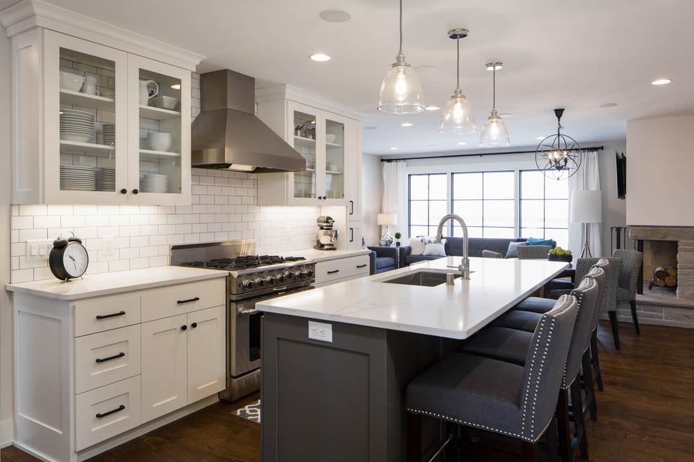 Inspiration for a transitional galley open plan kitchen in Minneapolis with an undermount sink, shaker cabinets, white cabinets, white splashback, subway tile splashback, stainless steel appliances, medium hardwood floors, with island, brown floor and white benchtop.