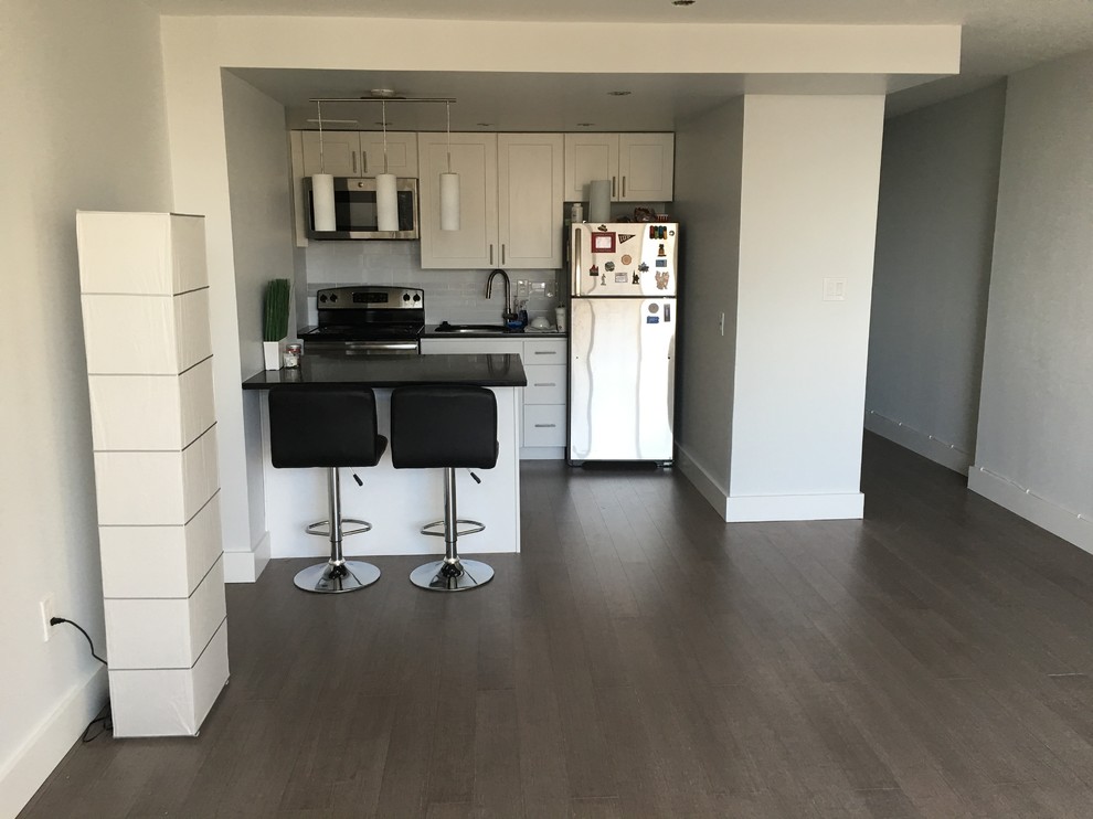 This is an example of a small contemporary single-wall eat-in kitchen in Philadelphia with a single-bowl sink, shaker cabinets, white cabinets, quartzite benchtops, white splashback, porcelain splashback, stainless steel appliances, bamboo floors and with island.