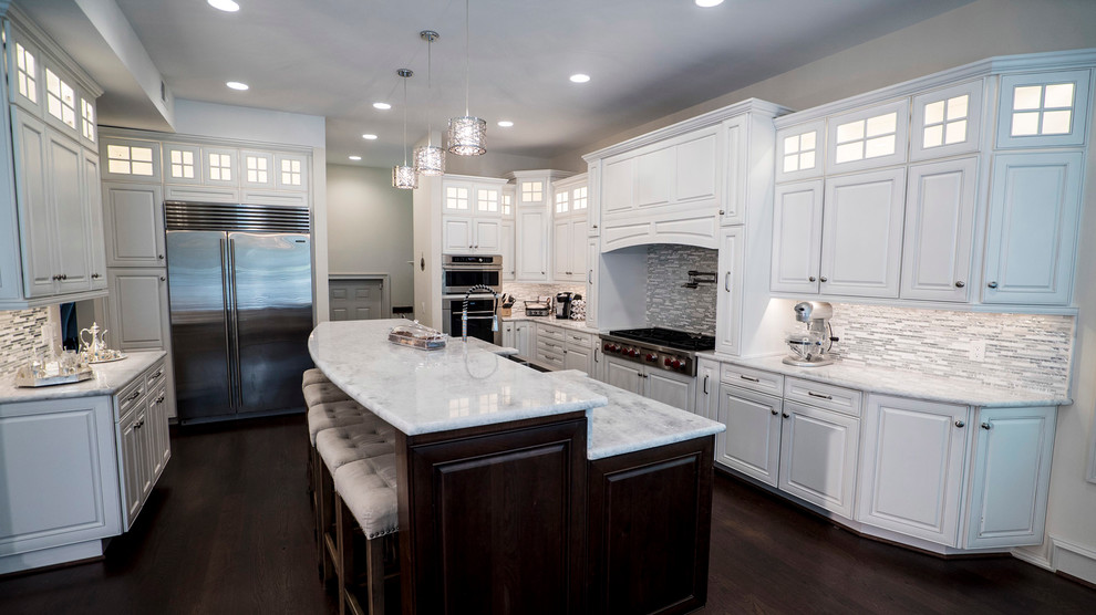 Large traditional single-wall open plan kitchen in DC Metro with a farmhouse sink, white cabinets, white splashback, stainless steel appliances, dark hardwood floors, with island, raised-panel cabinets, quartzite benchtops, porcelain splashback, brown floor and white benchtop.