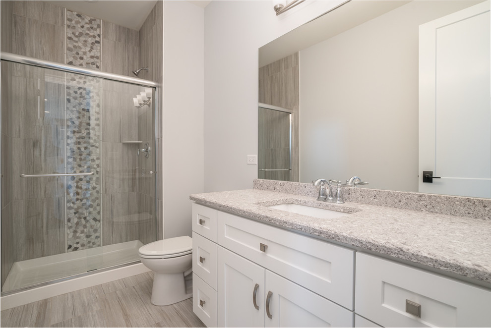 Mid-sized transitional kids bathroom in Chicago with white cabinets, a two-piece toilet, gray tile, porcelain tile, grey walls, porcelain floors, an undermount sink, grey floor, a sliding shower screen, recessed-panel cabinets, an alcove shower, terrazzo benchtops and grey benchtops.