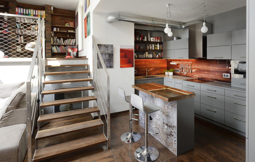 Mid-sized industrial l-shaped kitchen in Other with flat-panel cabinets, grey cabinets, granite benchtops, orange splashback, ceramic floors, with island, a single-bowl sink and brown floor.