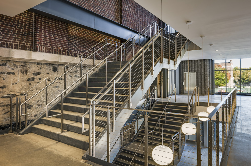 Cette image montre un très grand escalier droit design en béton avec des contremarches en béton, un garde-corps en câble et un mur en parement de brique.