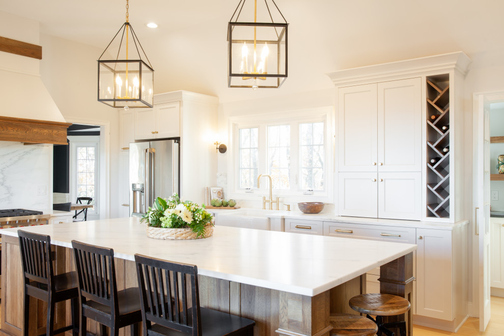 Photo of a large transitional l-shaped eat-in kitchen in Bridgeport with a farmhouse sink, recessed-panel cabinets, white cabinets, marble benchtops, white splashback, marble splashback, stainless steel appliances, light hardwood floors, with island and white benchtop.