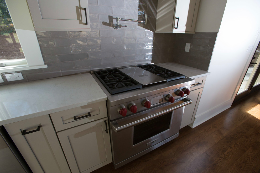 Inspiration for a mid-sized modern single-wall dark wood floor open concept kitchen remodel with an undermount sink, shaker cabinets, beige cabinets, quartz countertops, gray backsplash, ceramic backsplash, stainless steel appliances and an island