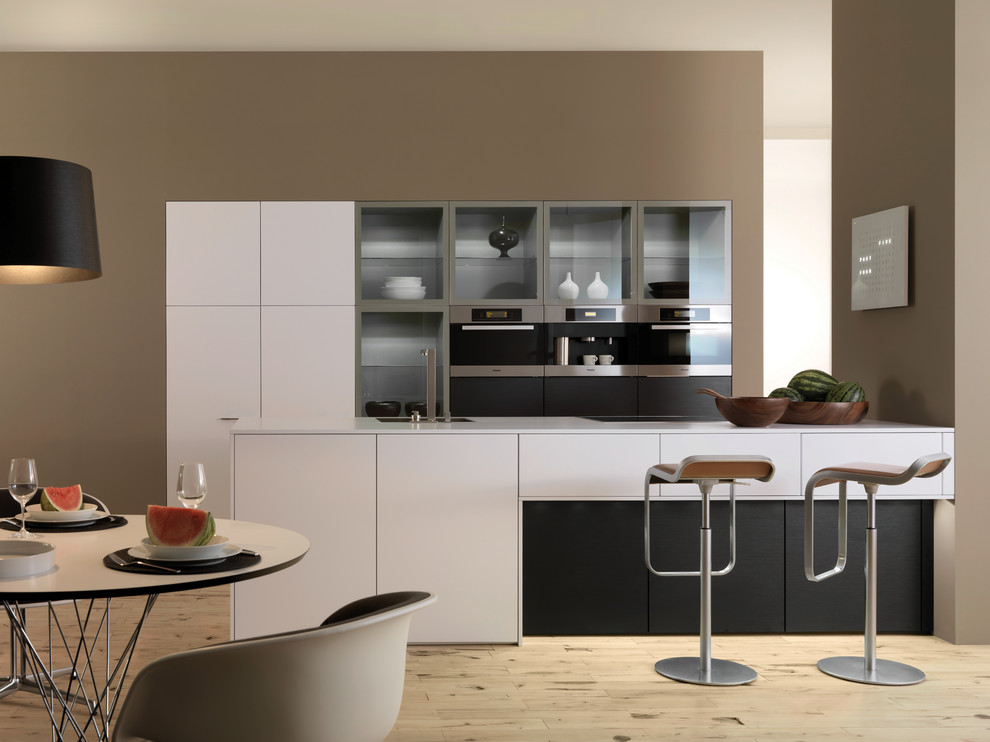 Design ideas for a mid-sized contemporary galley eat-in kitchen in New York with an undermount sink, flat-panel cabinets, white cabinets, solid surface benchtops, stainless steel appliances, light hardwood floors and a peninsula.