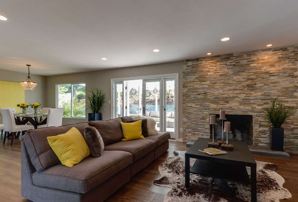 Photo of a mid-sized contemporary open concept living room in Los Angeles with beige walls, medium hardwood floors, a standard fireplace, a stone fireplace surround and a wall-mounted tv.