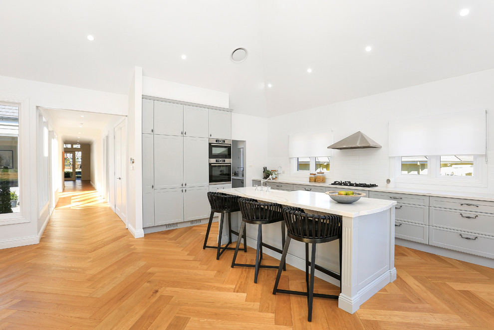 Inspiration for an expansive country galley open plan kitchen in Sydney with a farmhouse sink, shaker cabinets, grey cabinets, quartz benchtops, white splashback, ceramic splashback, stainless steel appliances, light hardwood floors, with island, multi-coloured floor and multi-coloured benchtop.