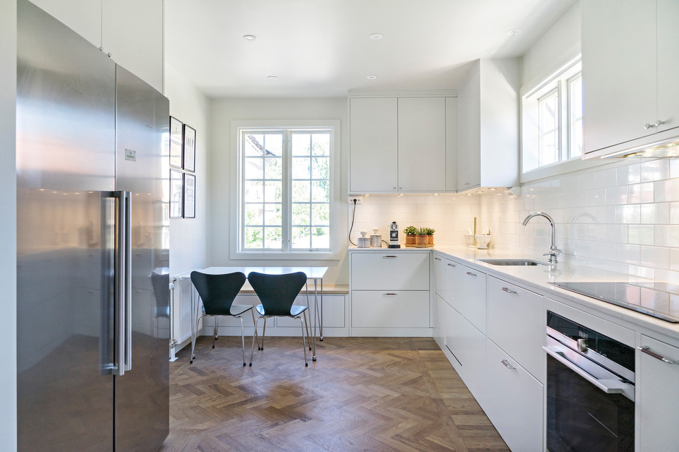 This is an example of a mid-sized contemporary single-wall kitchen in Stockholm with flat-panel cabinets, white cabinets and white splashback.