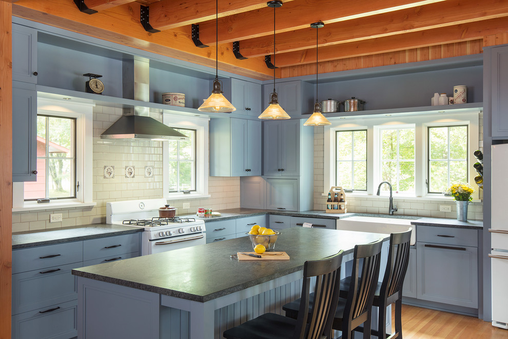 Inspiration for a country l-shaped kitchen in Minneapolis with a farmhouse sink, recessed-panel cabinets, blue cabinets, white splashback, subway tile splashback, white appliances, medium hardwood floors and with island.