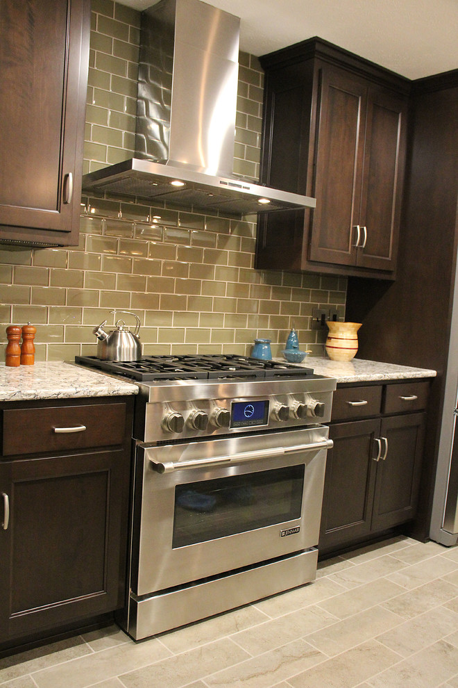 Mid-sized transitional l-shaped porcelain tile enclosed kitchen photo with a farmhouse sink, raised-panel cabinets, dark wood cabinets, quartz countertops, glass tile backsplash, stainless steel appliances and an island