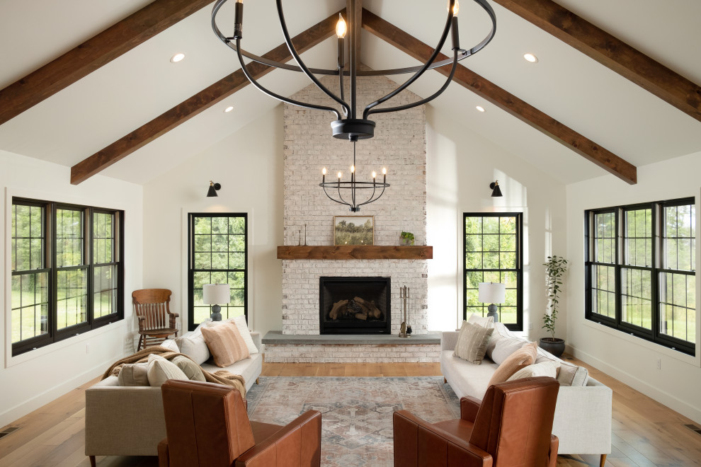 Idée de décoration pour un grand salon champêtre ouvert avec un mur blanc, parquet clair, une cheminée standard, un manteau de cheminée en brique, un sol beige et un plafond voûté.