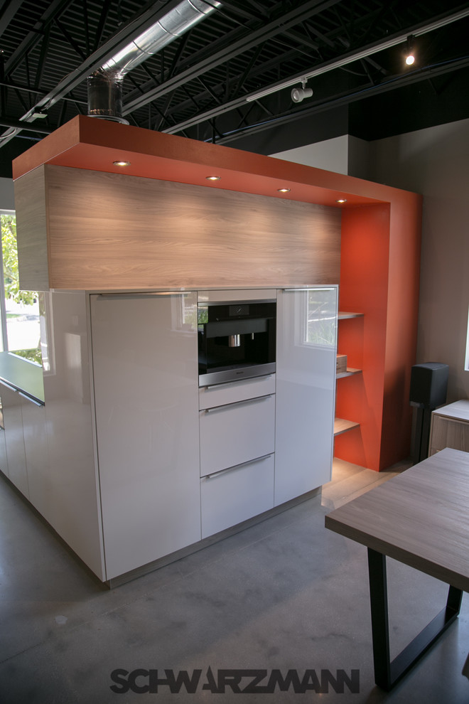 Mid-sized modern l-shaped open plan kitchen in Miami with an undermount sink, flat-panel cabinets, yellow cabinets, quartz benchtops, orange splashback, stone slab splashback, stainless steel appliances, concrete floors and a peninsula.