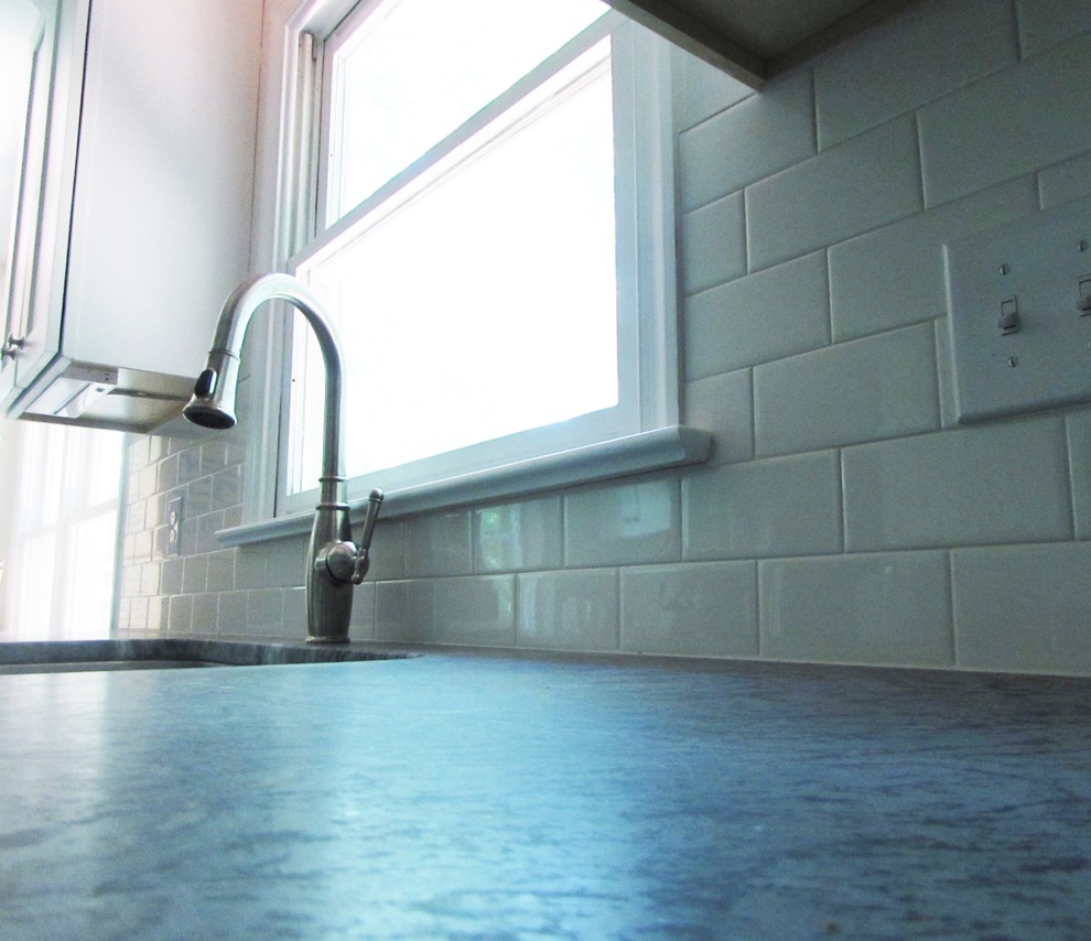 Mid-sized transitional l-shaped medium tone wood floor enclosed kitchen photo with an undermount sink, shaker cabinets, white cabinets, soapstone countertops, white backsplash, subway tile backsplash, stainless steel appliances and a peninsula