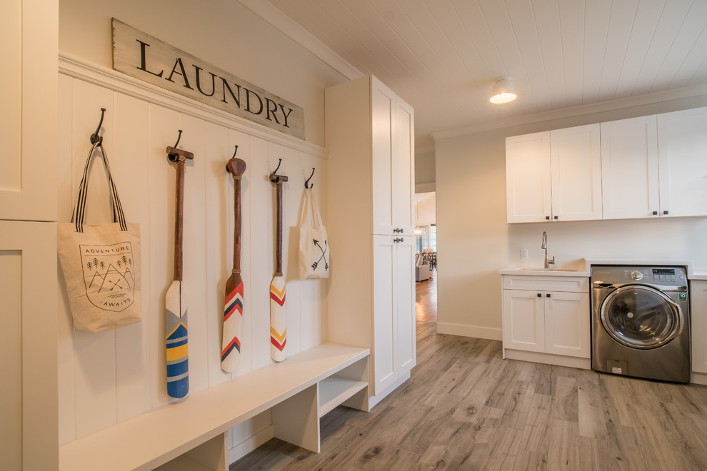 Design ideas for a large transitional l-shaped laundry room in Toronto with an undermount sink, shaker cabinets, white cabinets, solid surface benchtops, white walls, light hardwood floors and a side-by-side washer and dryer.