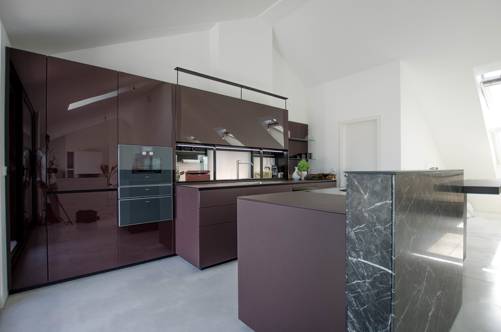 This is an example of an expansive contemporary galley eat-in kitchen in Berlin with a single-bowl sink, glass-front cabinets, purple cabinets, glass benchtops, glass sheet splashback, black appliances, concrete floors, with island, grey floor and purple benchtop.