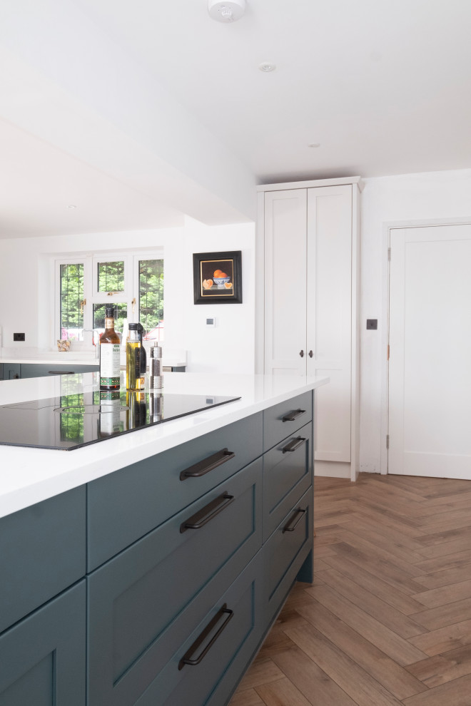 This is an example of a large traditional l-shaped kitchen in Cardiff with an integrated sink, shaker cabinets, light wood cabinets, quartzite benchtops, stainless steel appliances, laminate floors, with island and white benchtop.