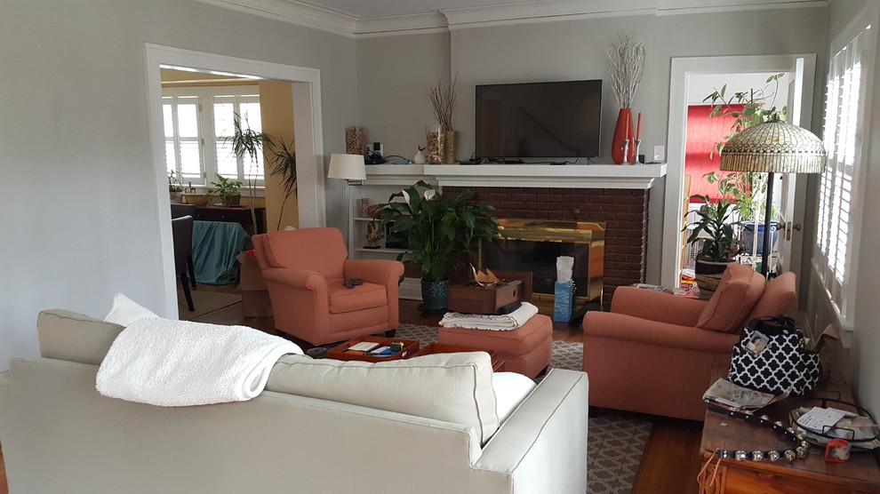 Photo of a mid-sized traditional enclosed living room in Kansas City with grey walls, medium hardwood floors, a standard fireplace, a brick fireplace surround, a wall-mounted tv and brown floor.