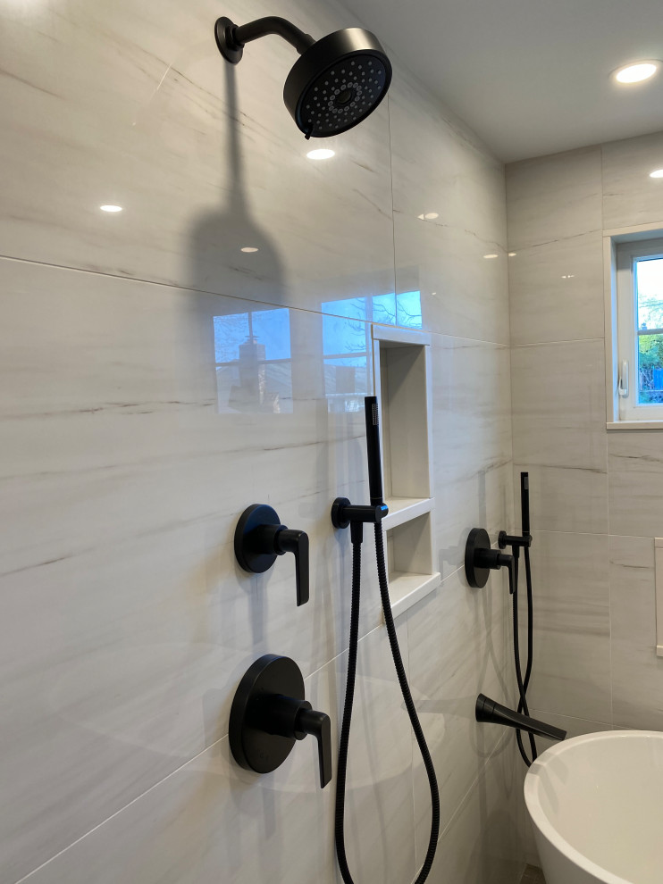 Пример оригинального дизайна: большая главная, серо-белая ванная комната в стиле неоклассика (современная классика) с плоскими фасадами, светлыми деревянными фасадами, отдельно стоящей ванной, душевой комнатой, унитазом-моноблоком, белой плиткой, керамогранитной плиткой, белыми стенами, полом из керамогранита, врезной раковиной, столешницей из искусственного кварца, серым полом, душем с распашными дверями, белой столешницей, тумбой под две раковины и подвесной тумбой