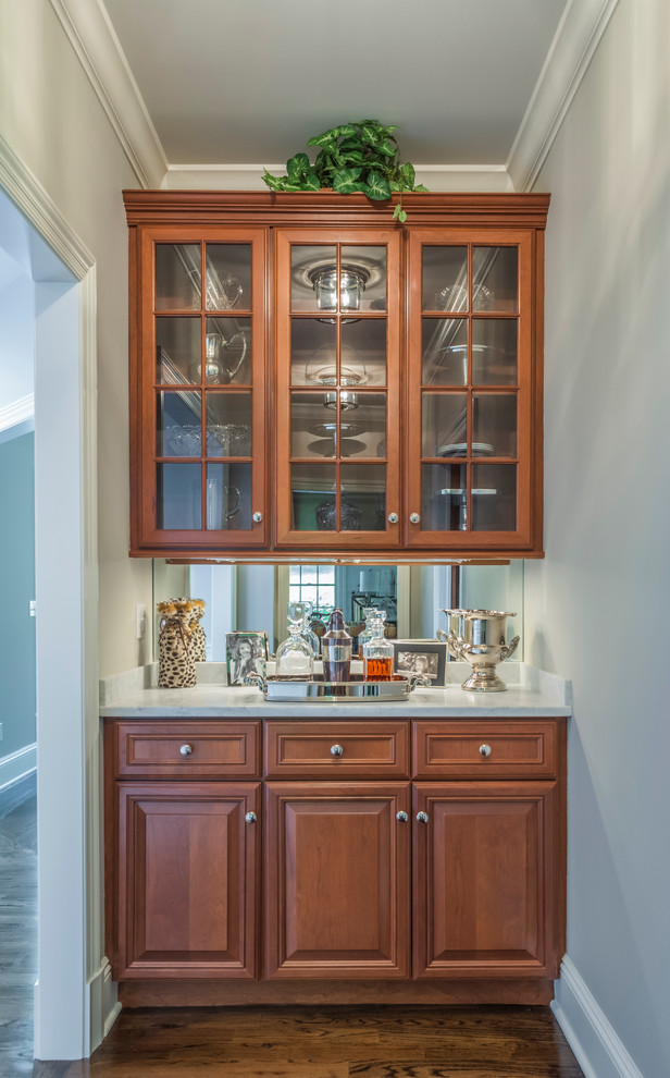 Photo of a small traditional single-wall wet bar in New York with raised-panel cabinets, medium wood cabinets, solid surface benchtops and dark hardwood floors.