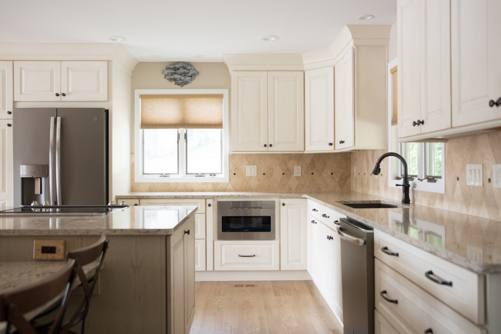 Transitional u-shaped light wood floor eat-in kitchen photo with an undermount sink, raised-panel cabinets, white cabinets, beige backsplash, stainless steel appliances, an island and beige countertops