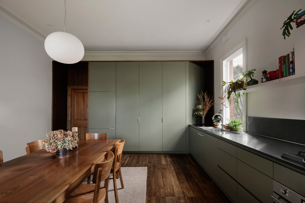 Contemporary l-shaped eat-in kitchen in Melbourne with a double-bowl sink, flat-panel cabinets, green cabinets, panelled appliances, dark hardwood floors, no island, brown floor and black benchtop.