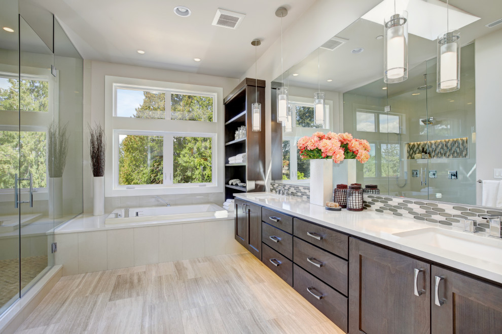 This is an example of a large transitional master bathroom in Orange County with shaker cabinets, white tile, porcelain tile, porcelain floors, solid surface benchtops, dark wood cabinets, a drop-in tub, an alcove shower, grey walls, an undermount sink, grey floor, a hinged shower door, white benchtops, a double vanity and a floating vanity.