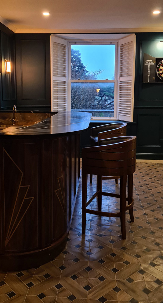This is an example of a large midcentury u-shaped home bar in Dublin with a drop-in sink, medium wood cabinets, copper benchtops, black splashback, porcelain floors, multi-coloured floor and black benchtop.