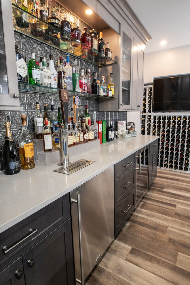 Design ideas for a small industrial u-shaped seated home bar in DC Metro with an undermount sink, shaker cabinets, medium wood cabinets, quartz benchtops, grey splashback, metal splashback, vinyl floors, brown floor and grey benchtop.