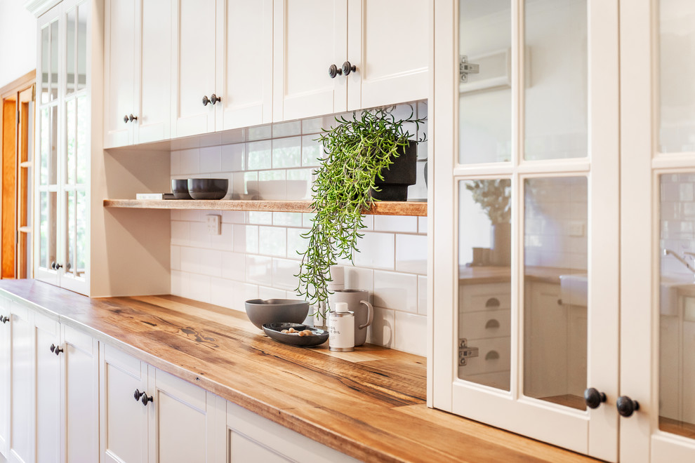 Inspiration for a mid-sized country l-shaped eat-in kitchen in Adelaide with a farmhouse sink, shaker cabinets, white cabinets, wood benchtops, white splashback, subway tile splashback, black appliances, slate floors, a peninsula, grey floor and yellow benchtop.
