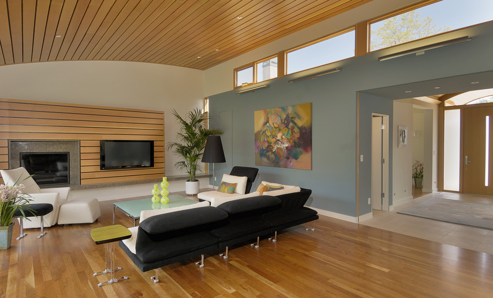 Design ideas for a mid-sized contemporary family room in San Francisco with a wood fireplace surround, wood, multi-coloured walls, light hardwood floors, a wall-mounted tv and brown floor.