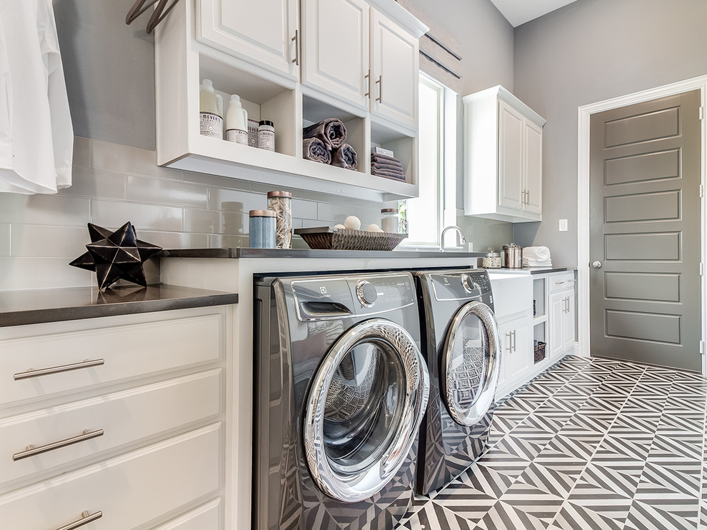 Inspiration for a mid-sized modern galley utility room in Dallas with a farmhouse sink, raised-panel cabinets, white cabinets, grey walls, ceramic floors, a side-by-side washer and dryer, multi-coloured floor and grey benchtop.