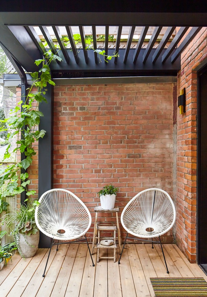 This is an example of a small scandinavian backyard deck in Toronto with a container garden and a pergola.