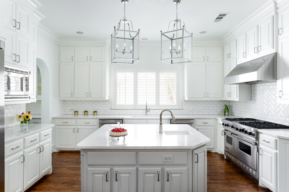Example of a mid-sized classic medium tone wood floor and brown floor enclosed kitchen design in Dallas with an undermount sink, raised-panel cabinets, white cabinets, quartz countertops, white backsplash, stainless steel appliances, an island, white countertops and subway tile backsplash