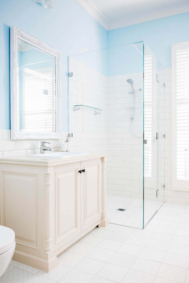 This is an example of a small traditional master bathroom in Melbourne with furniture-like cabinets, white cabinets, a curbless shower, a two-piece toilet, white tile, ceramic tile, white walls, ceramic floors, a drop-in sink, engineered quartz benchtops, a hinged shower door and white floor.