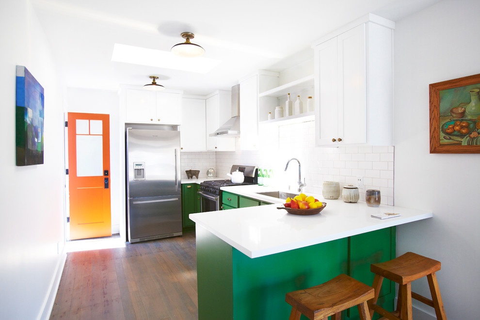This is an example of an eclectic l-shaped kitchen in Los Angeles with shaker cabinets, green cabinets, white splashback, subway tile splashback and stainless steel appliances.