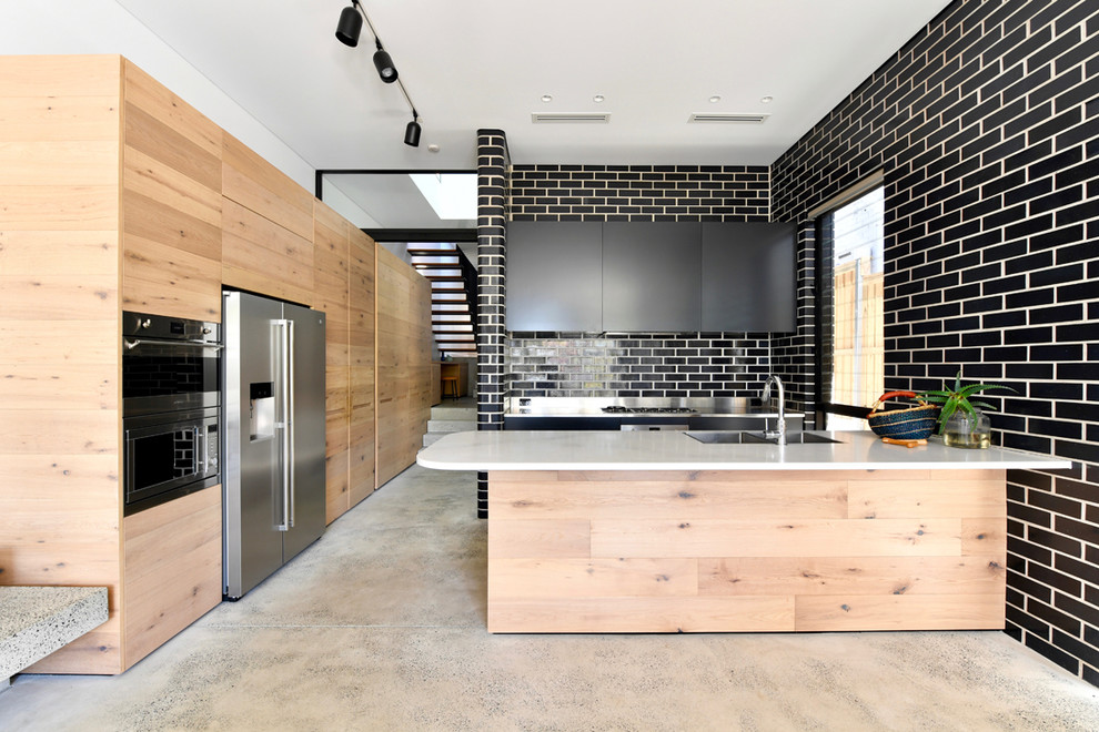 Photo of a mid-sized contemporary galley open plan kitchen in Sydney with flat-panel cabinets, light wood cabinets, black splashback, subway tile splashback, stainless steel appliances, concrete floors, with island and grey floor.