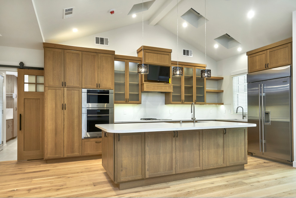 Amerikansk inredning av ett mellanstort vit vitt kök, med en undermonterad diskho, skåp i shakerstil, skåp i mellenmörkt trä, vitt stänkskydd, rostfria vitvaror, mellanmörkt trägolv, en köksö och brunt golv