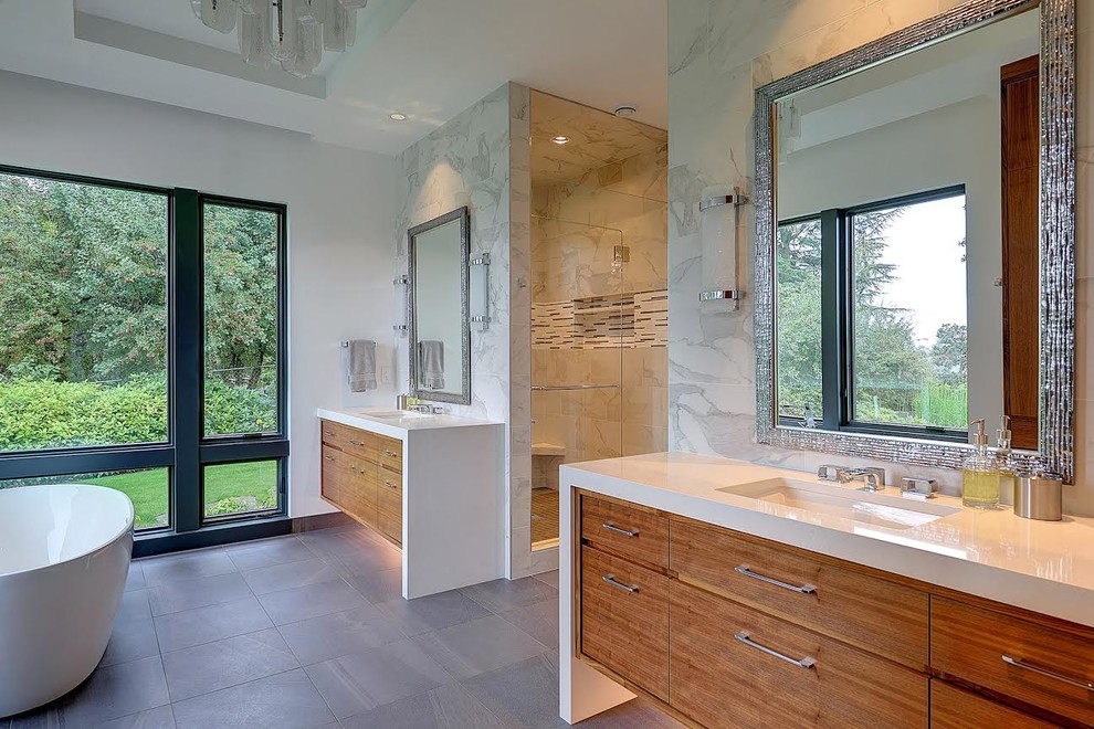 This is an example of a large contemporary master bathroom in Portland with flat-panel cabinets, medium wood cabinets, a freestanding tub, an alcove shower, gray tile, multi-coloured tile, white walls, slate floors, an undermount sink, engineered quartz benchtops, grey floor, a hinged shower door, white benchtops and marble.