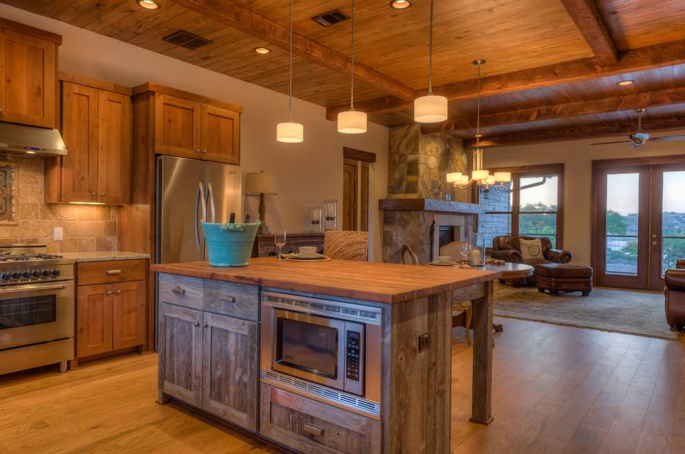 This is an example of a large country l-shaped eat-in kitchen in Austin with stainless steel appliances, wood benchtops, an undermount sink, shaker cabinets, medium wood cabinets and with island.