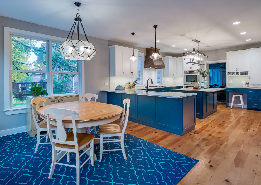 Photo of a large country l-shaped eat-in kitchen in Chicago with a farmhouse sink, shaker cabinets, turquoise cabinets, marble benchtops, white splashback, porcelain splashback, stainless steel appliances, light hardwood floors, with island, brown floor, multi-coloured benchtop and wallpaper.