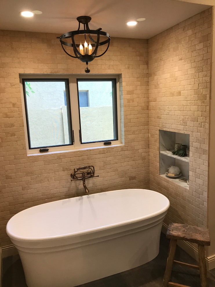 Photo of a mid-sized mediterranean master bathroom in Phoenix with raised-panel cabinets, dark wood cabinets, a freestanding tub, an alcove shower, a one-piece toilet, beige tile, stone tile, beige walls, dark hardwood floors, a vessel sink, marble benchtops, brown floor and a hinged shower door.