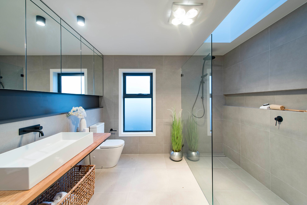 Design ideas for a mid-sized beach style master bathroom in Canberra - Queanbeyan with a freestanding tub, gray tile, ceramic tile, a corner shower, a one-piece toilet, grey walls, a vessel sink, wood benchtops, beige floor, an open shower and beige benchtops.