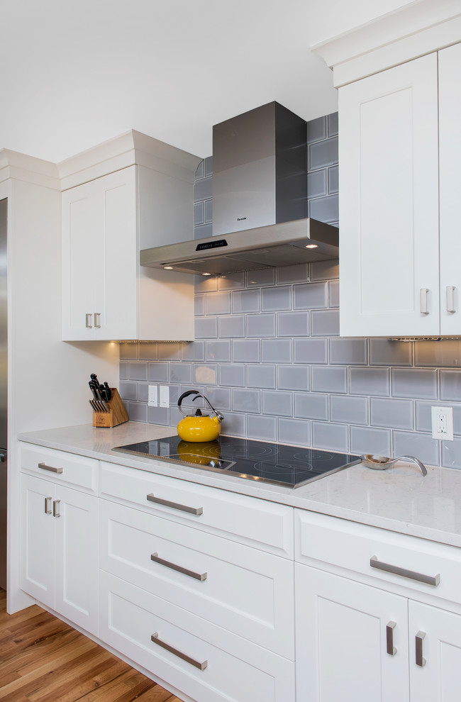 Inspiration for a large transitional u-shaped light wood floor enclosed kitchen remodel in Denver with a farmhouse sink, shaker cabinets, white cabinets, quartz countertops, gray backsplash, ceramic backsplash, stainless steel appliances and an island