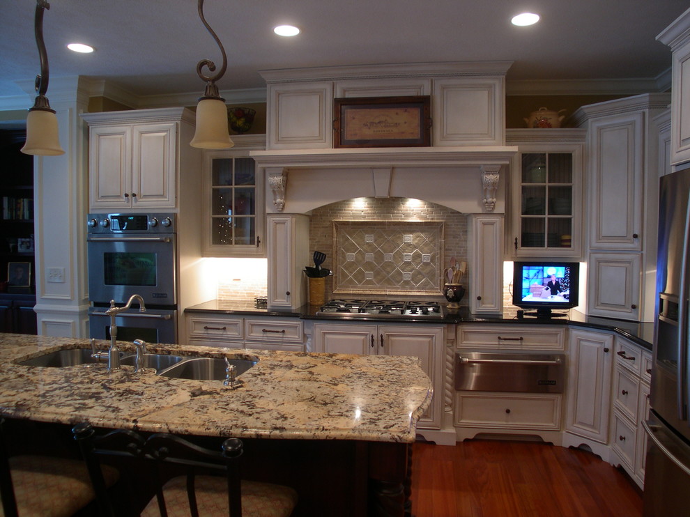 This is an example of a large traditional l-shaped eat-in kitchen in Indianapolis with a triple-bowl sink, recessed-panel cabinets, white cabinets, granite benchtops, beige splashback, stone tile splashback, stainless steel appliances and with island.