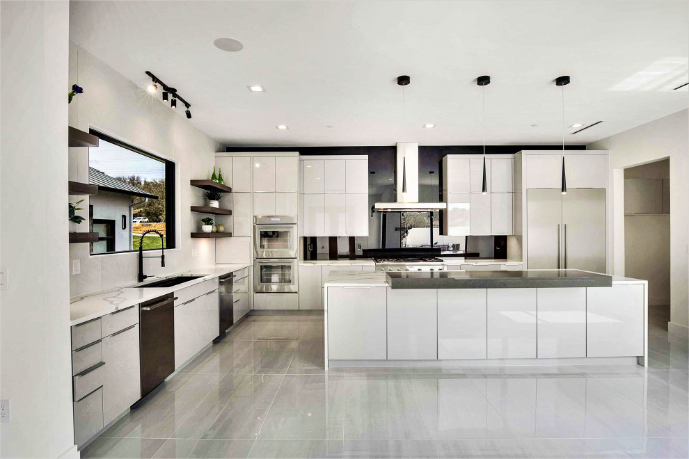 Große Moderne Küche in grau-weiß in L-Form mit Einbauwaschbecken, flächenbündigen Schrankfronten, grauen Schränken, Quarzwerkstein-Arbeitsplatte, Küchenrückwand in Schwarz, Glasrückwand, Küchengeräten aus Edelstahl, Porzellan-Bodenfliesen, Kücheninsel, weißem Boden und weißer Arbeitsplatte in Austin