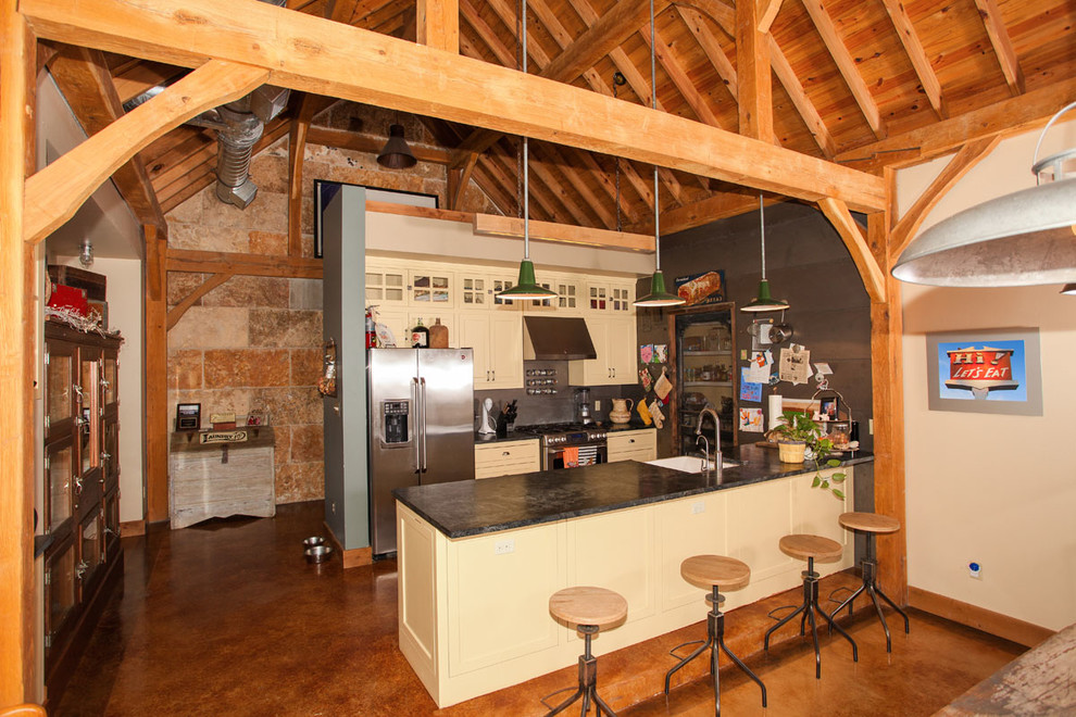 Mid-sized mountain style galley open concept kitchen photo in Austin with a farmhouse sink, recessed-panel cabinets, yellow cabinets, gray backsplash, stainless steel appliances and a peninsula